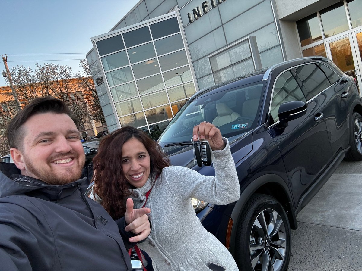 Couple smiling and holding car keys in front of a new vehicle at the dealership