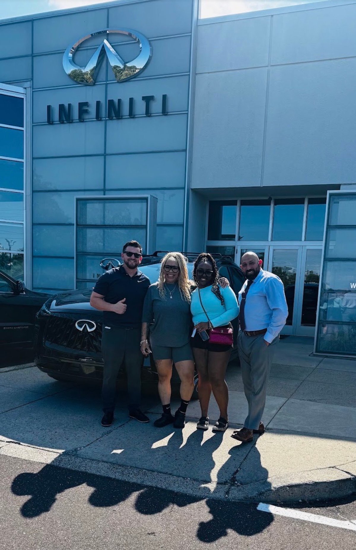 Nick with clients and team members, all smiles in front of a black INFINITI at the Faulkner dealership