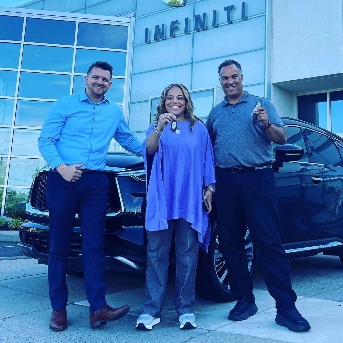 Three people smiling at the INFINITI dealership with luxury vehicles and the building in the background