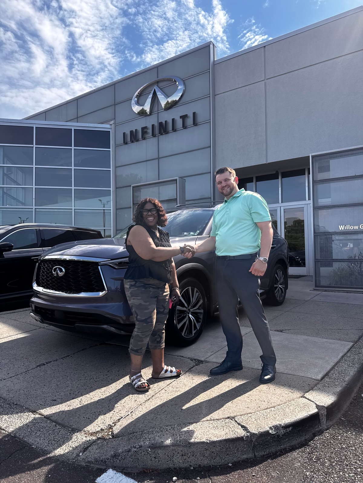 Two people shaking hands in front of a black Infiniti vehicle at an Infiniti dealership