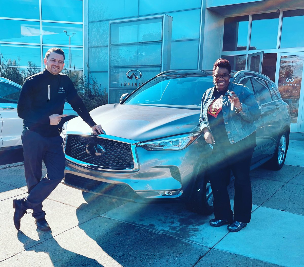 Two people standing beside a silver and teal SUV in front of a modern glass building with blue tinting